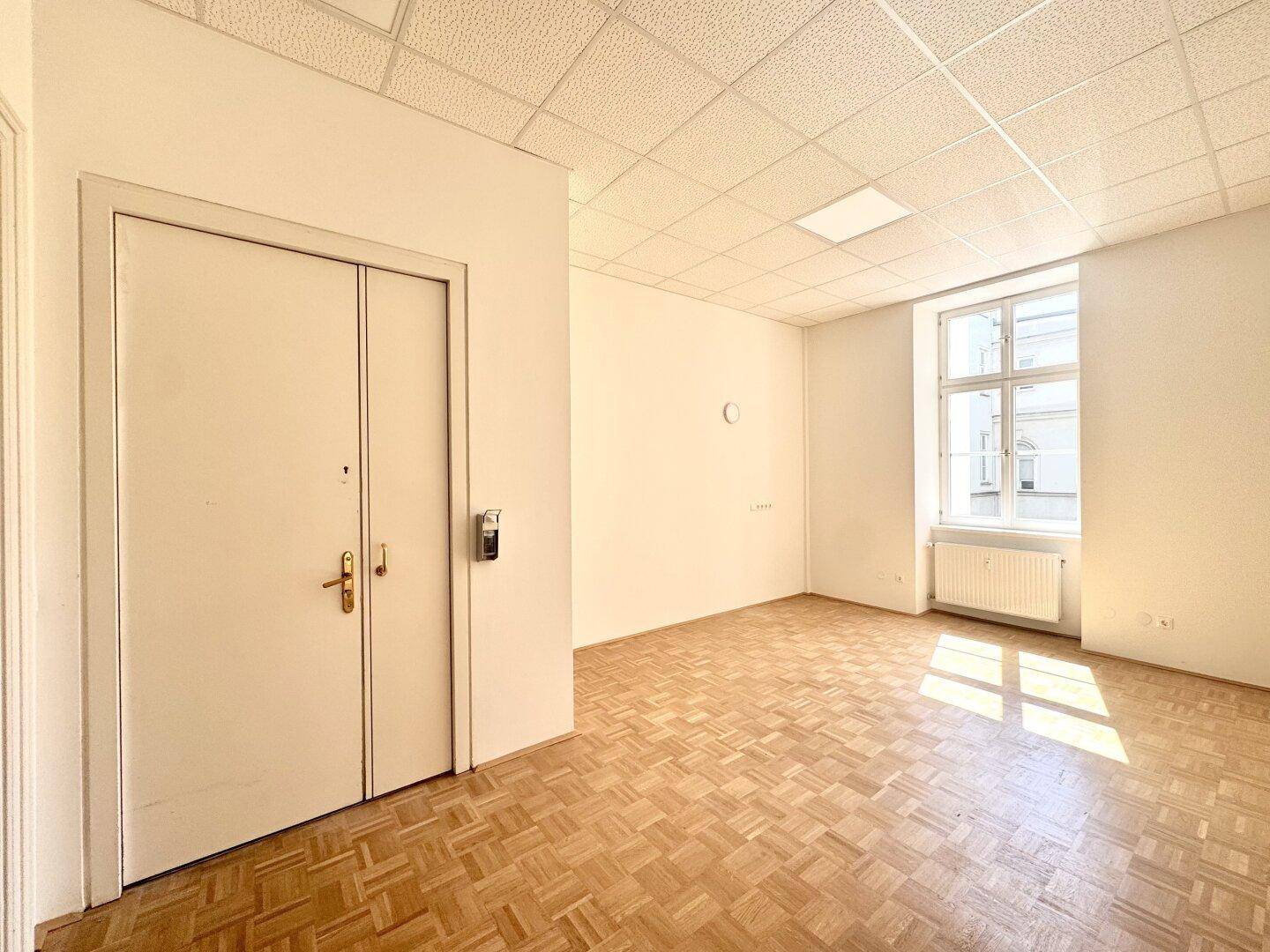 Geräumiger Raum mit Parkettboden und einem Fenster, das viel Tageslicht hereinlässt.