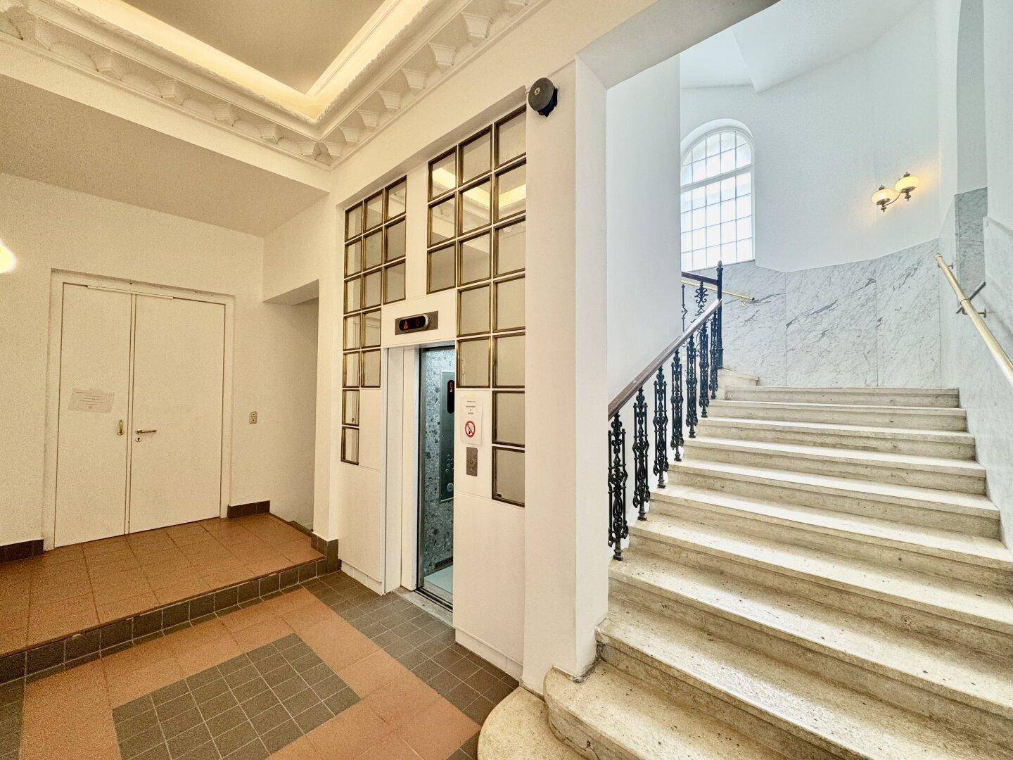 Elegantes Treppenhaus mit Marmorverkleidung, schmiedeeisernem Geländer und einem modernen Aufzug.
