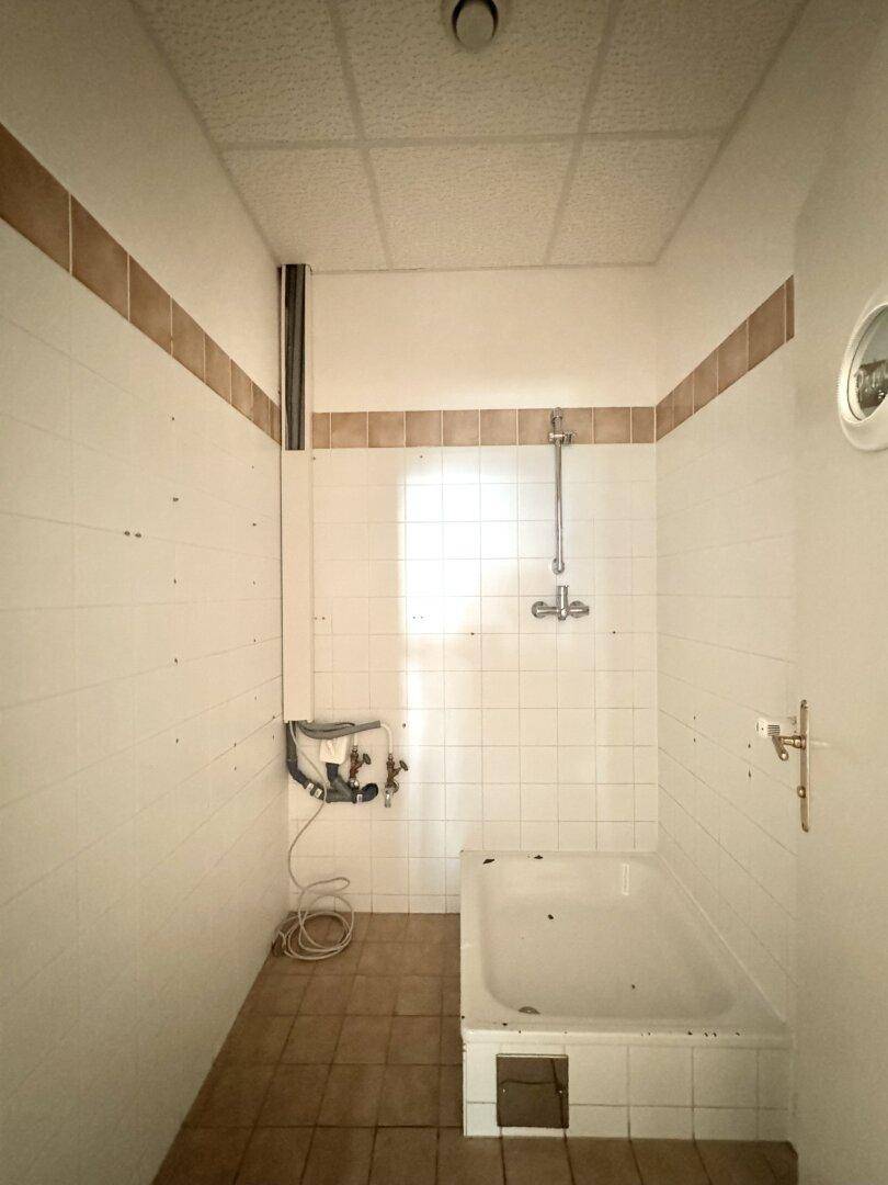 Einfacher Duschbereich mit Fliesenwänden und einer Badewanne, bereit zur Nutzung.