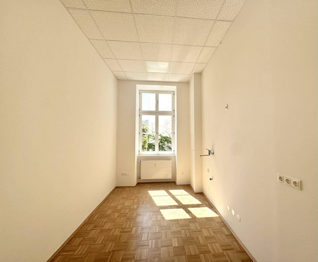 Heller Raum mit Parkettboden und einem Fenster, das viel natürliches Licht bietet.