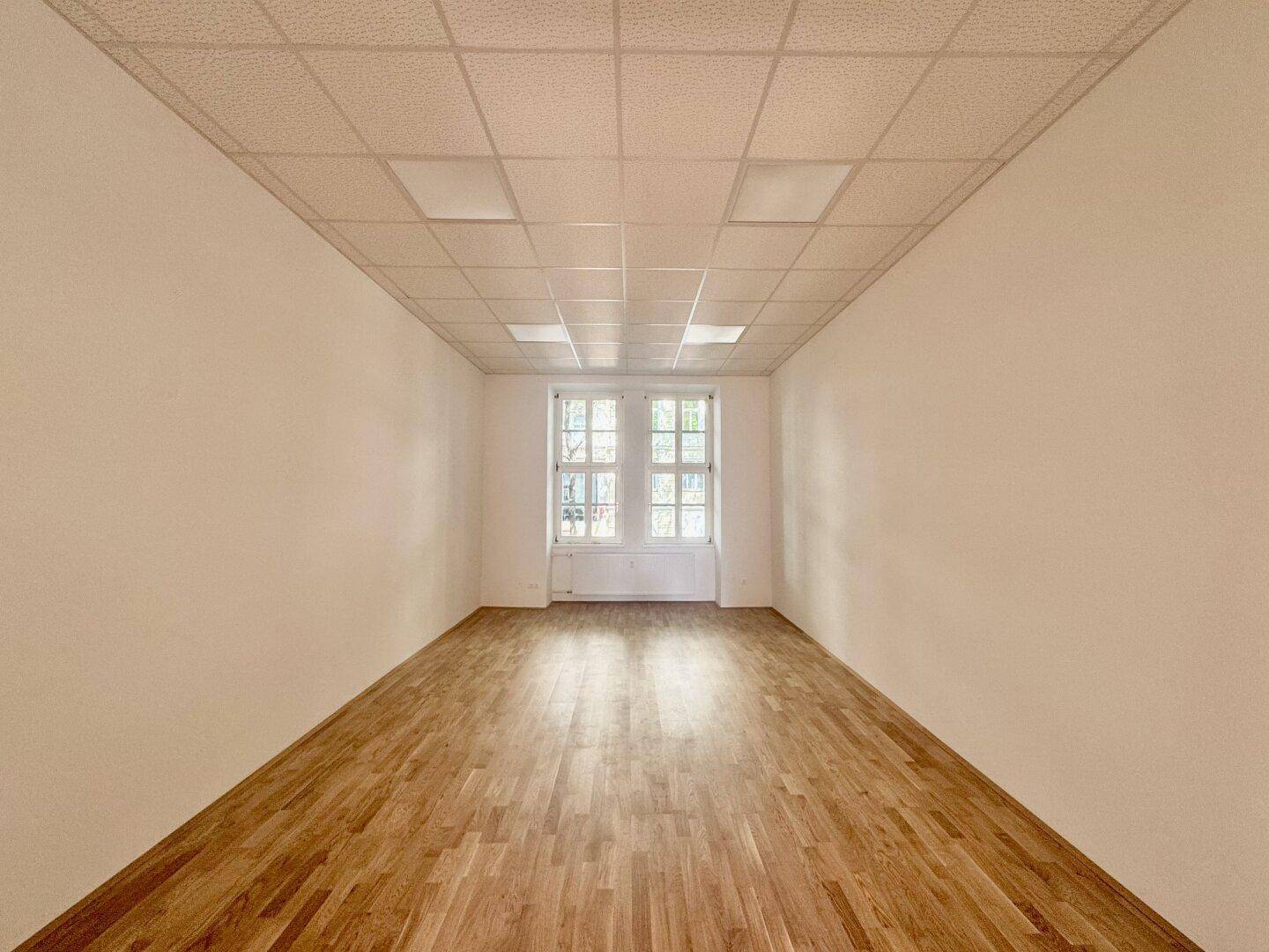 Langer, schmaler Raum mit Holzboden und einem Fenster am Ende, geeignet für Büro oder Praxis.