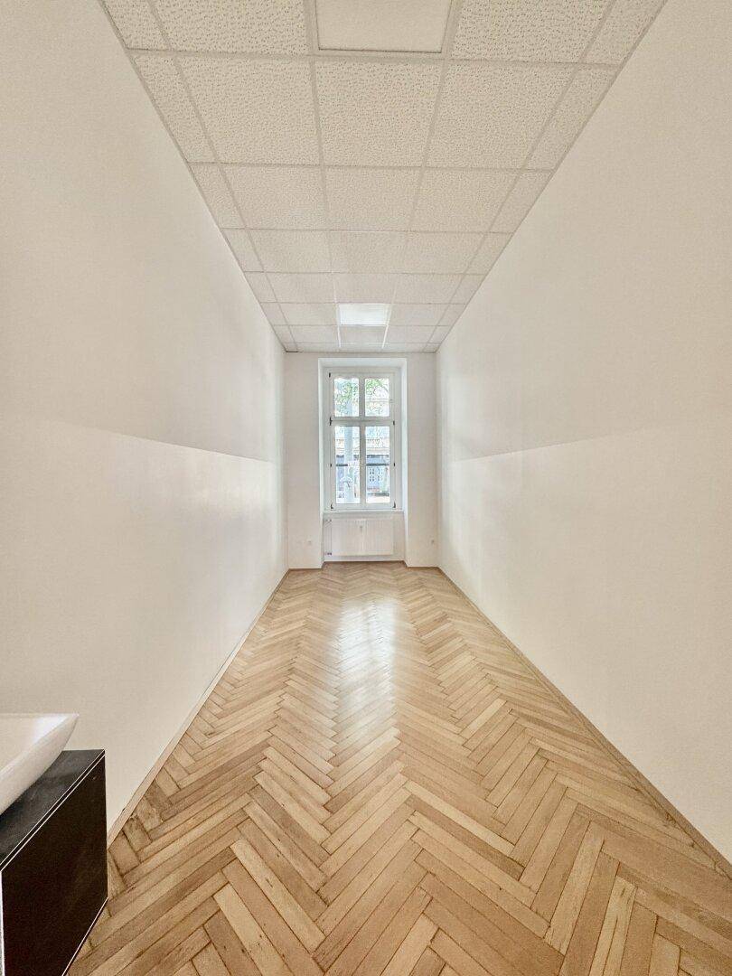 Schmaler Raum mit Fischgrätparkett und einem Fenster, bietet vielseitige Nutzungsmöglichkeiten.