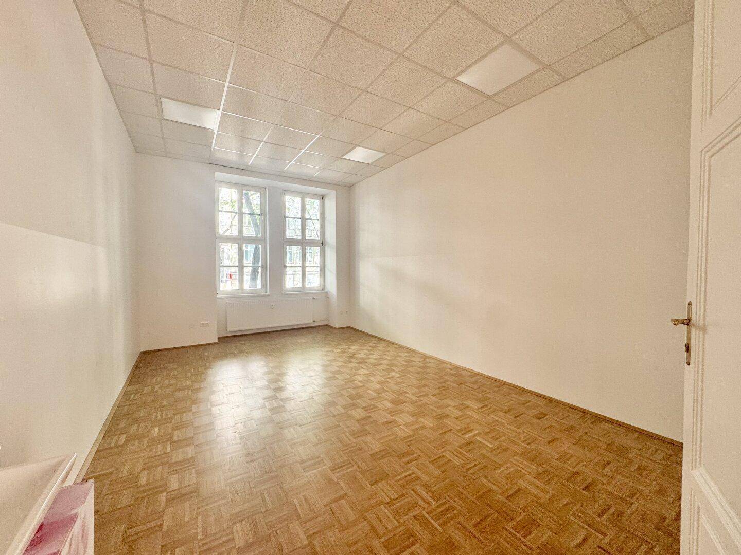 Leerer Raum mit Parkettboden und zwei Fenstern, bereit für individuelle Gestaltung.