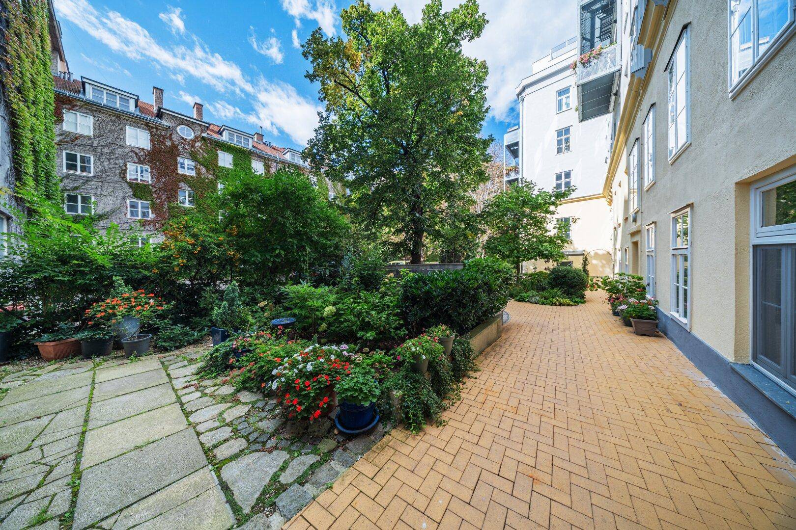 Gepflegter Innenhofgarten mit üppigem Grün, Bäumen, Blumenbeeten und gepflasterten Wegen.