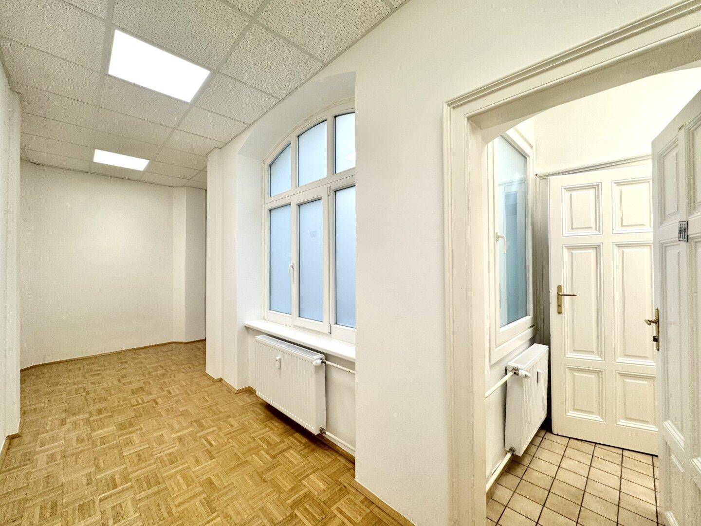 Heller Flur mit Parkettboden, einem Bogenfenster und Heizkörpern unter der Fensterbank.