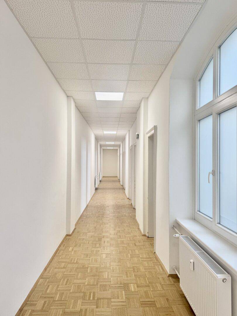 Langer, heller Flur mit Parkettboden, weißen Wänden und mehreren Türen auf beiden Seiten.