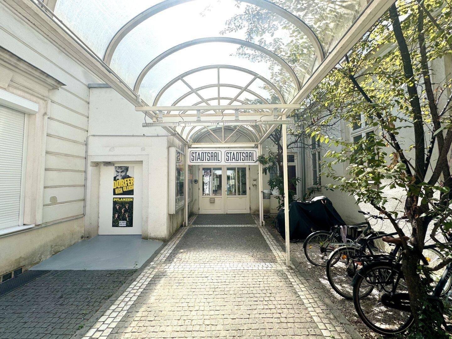 Eingangsbereich eines Gebäudes mit einer modernen Glasüberdachung und Beschilderung.