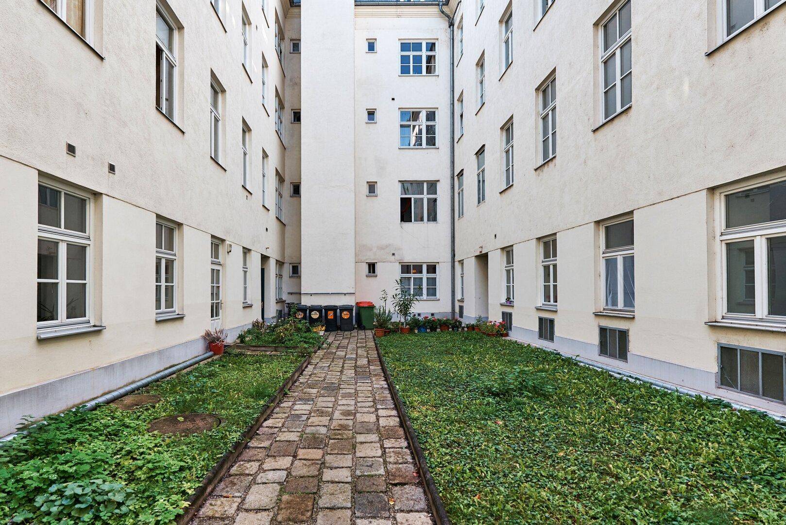 Grüner Innenhof mit gepflastertem Weg und umliegenden Gebäudefassaden.