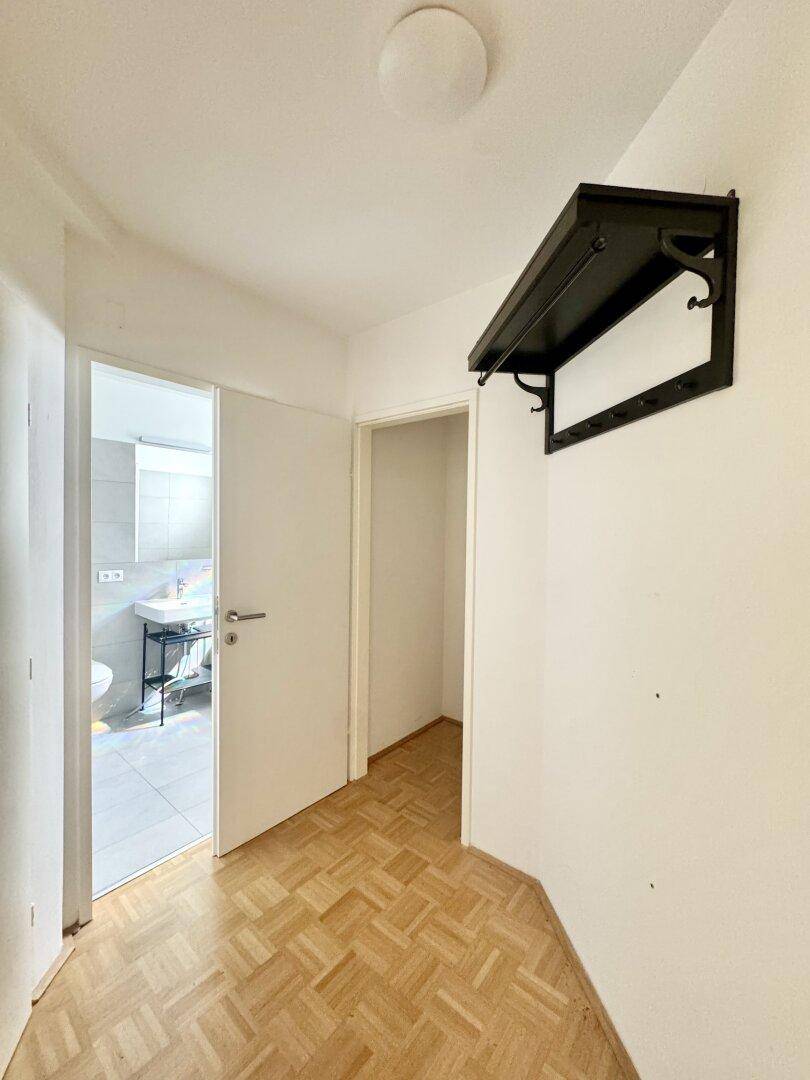 Heller Flur mit Parkettboden und Garderobe, der zu weiteren Räumen führt.