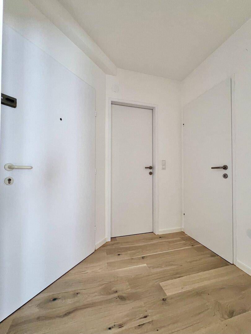 Heller Flur mit hellem Holzparkett und mehreren weißen Türen, die zu den Zimmern führen.