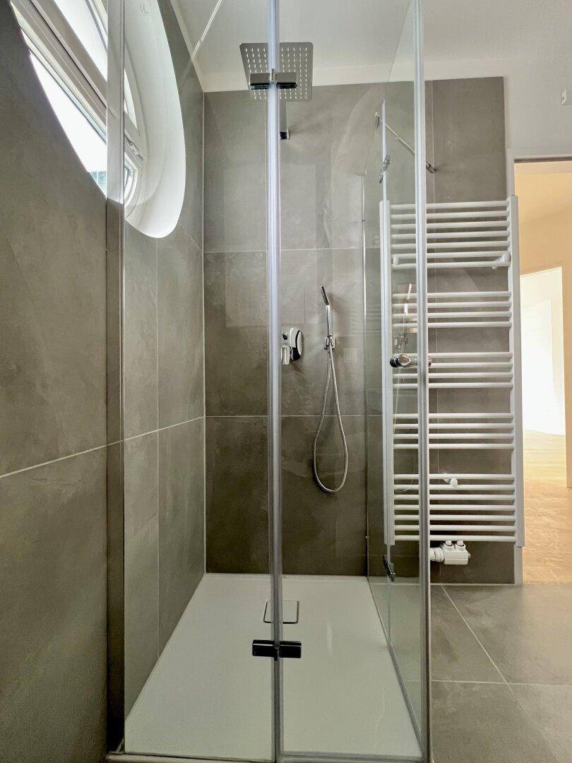 Geräumige Duschkabine mit Regendusche, Glasabtrennung und beheiztem Handtuchhalter im modernen Bad.