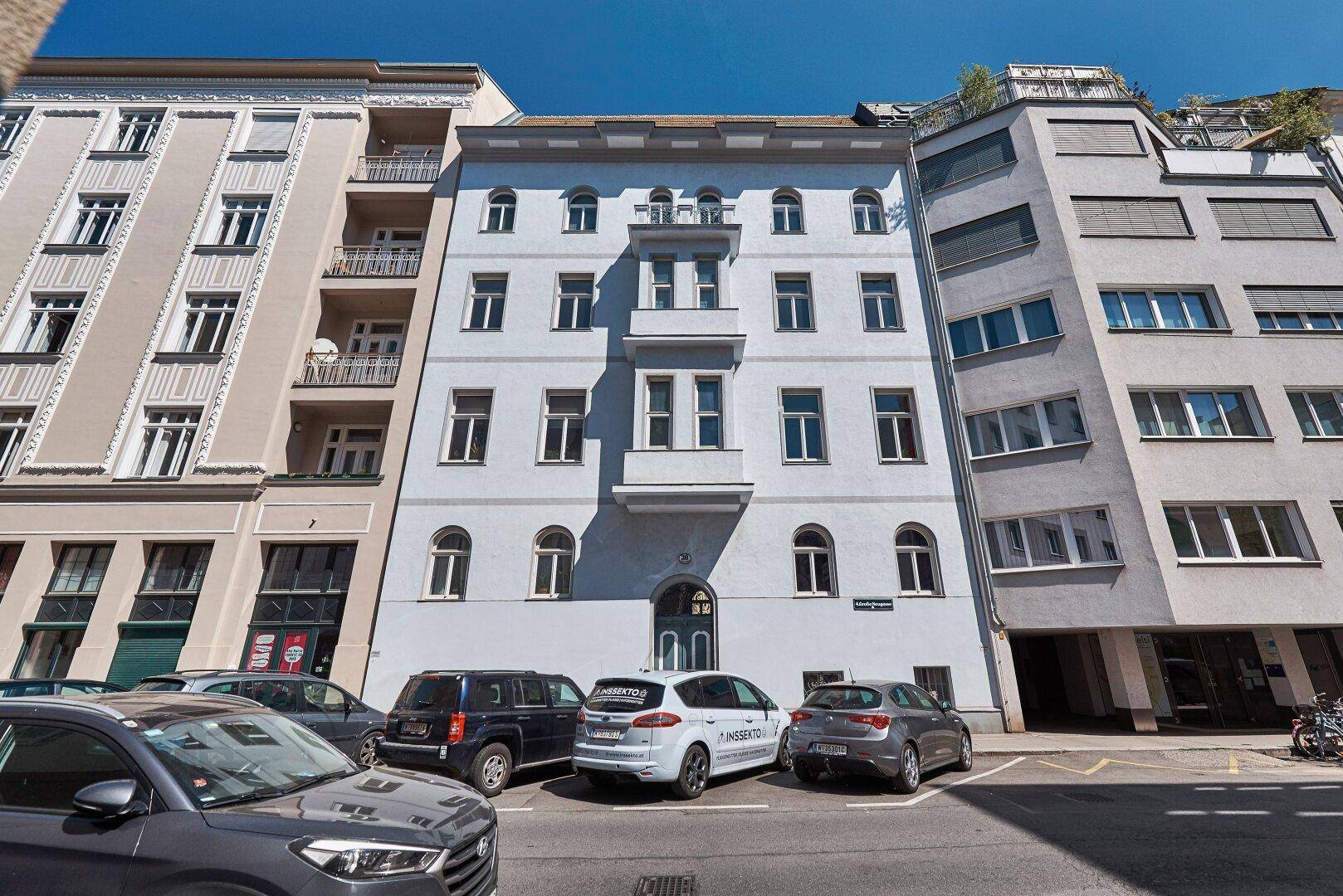 Historisches Gebäude mit klassischer Fassade und geparkten Autos auf der Straße davor.