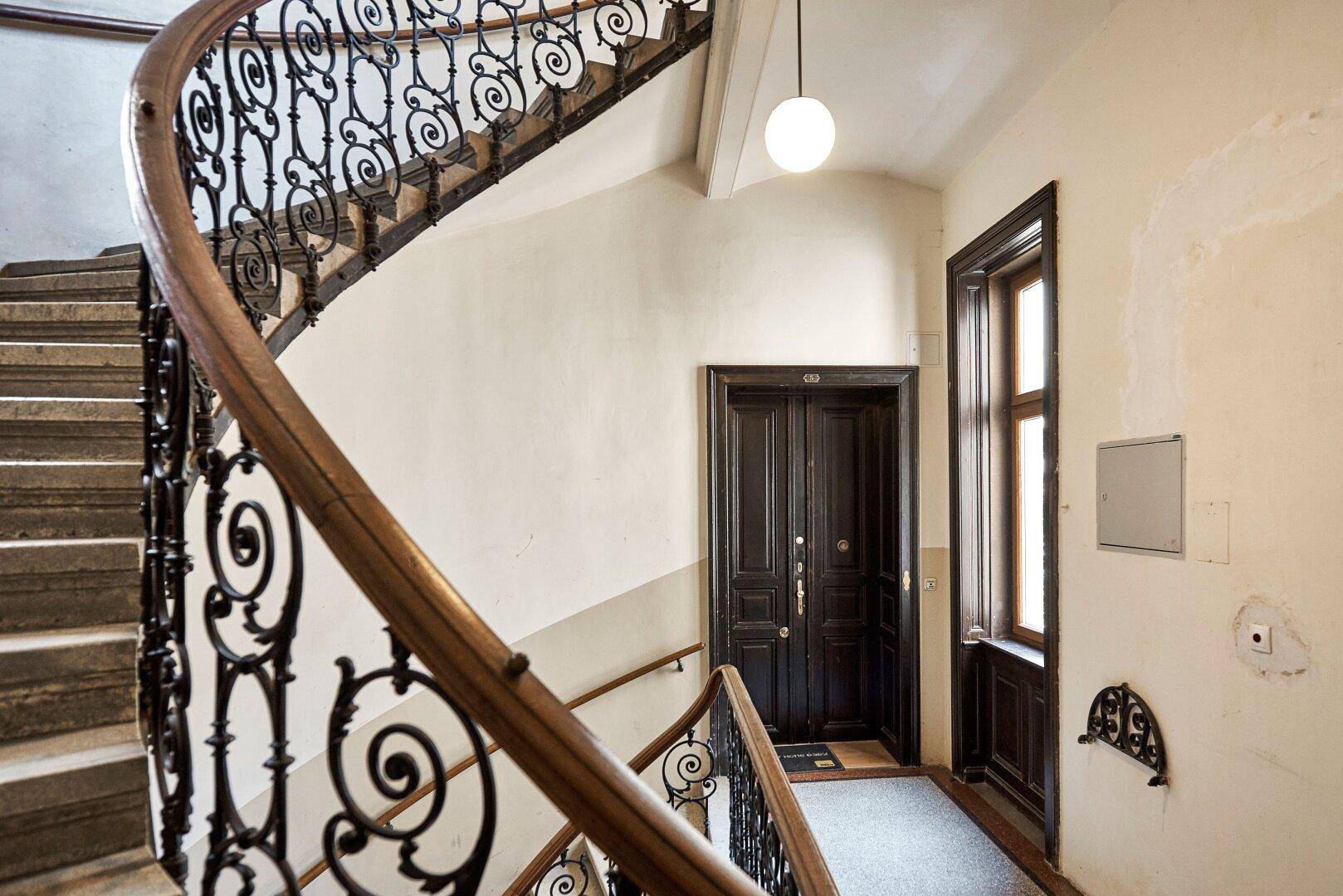 Geschwungenes Treppenhaus mit kunstvollem schmiedeeisernem Geländer und Holzhandlauf in einem Altbau.