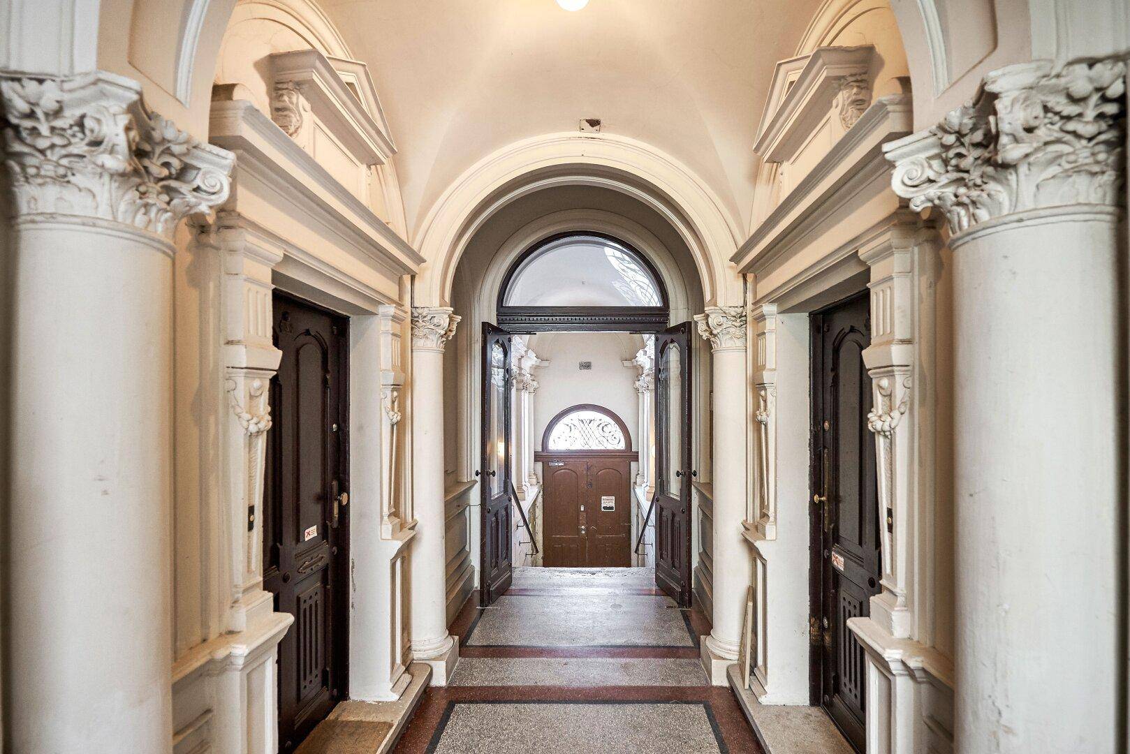 Prunkvoller Eingangsbereich mit hohen Säulen, Bögen und verzierten Türen im Altbau.