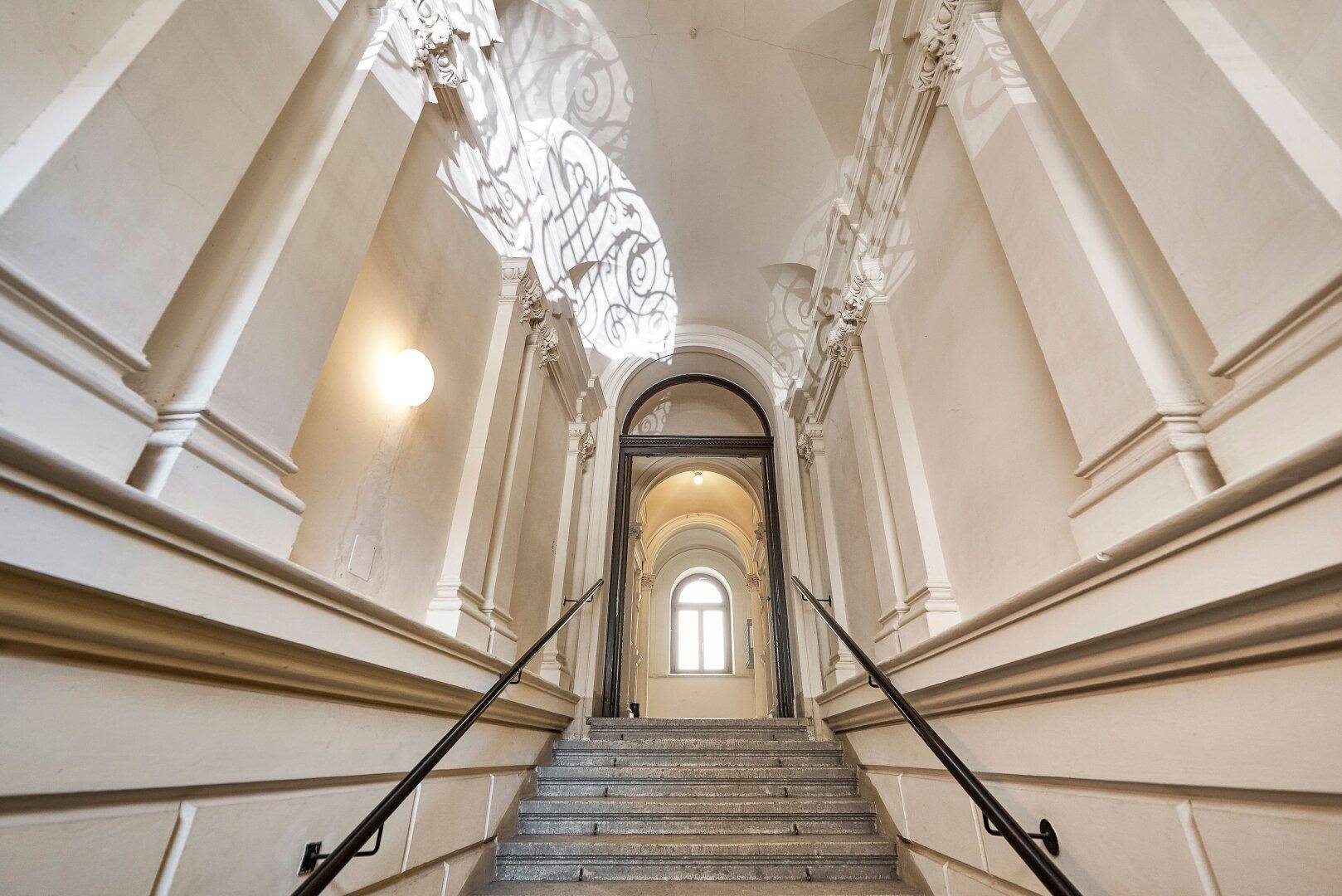 Elegantes Treppenhaus mit geschwungenen Geländern und hohen Decken, das zu den oberen Etagen führt.