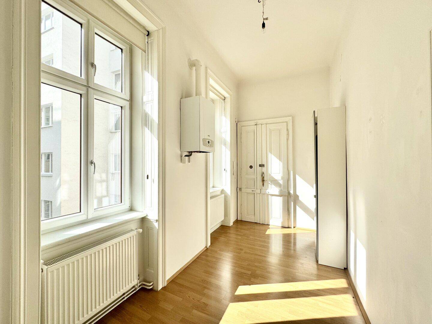 Heller Flur mit Fischgrätparkettboden und einem Heizkessel an der Wand, der viel Sonnenlicht empfängt.