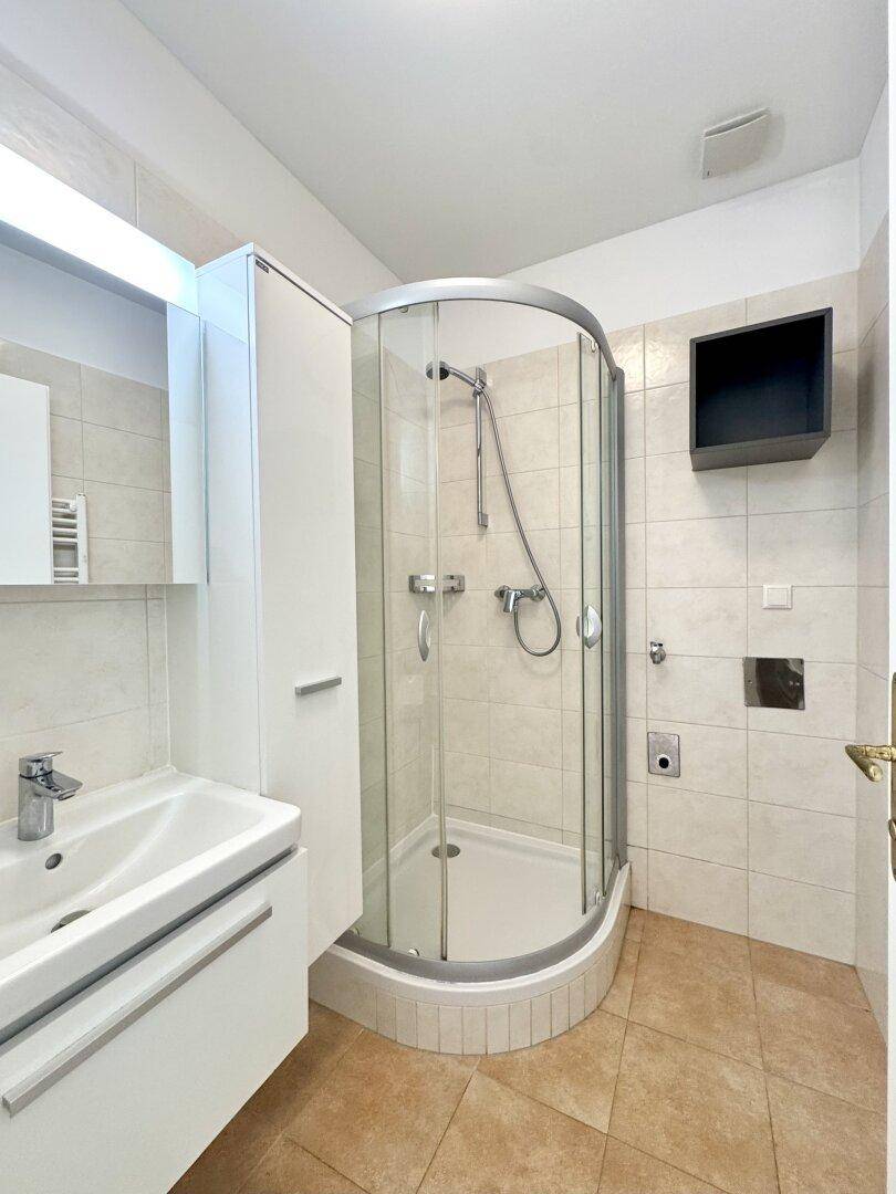 Helles Badezimmer mit Duschkabine, Waschbecken und Spiegelschrank, komplett gefliest.