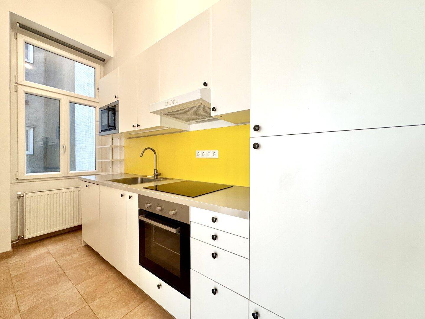 Moderne Einbauküche mit weißen Schränken, gelber Rückwand und integrierten Geräten.