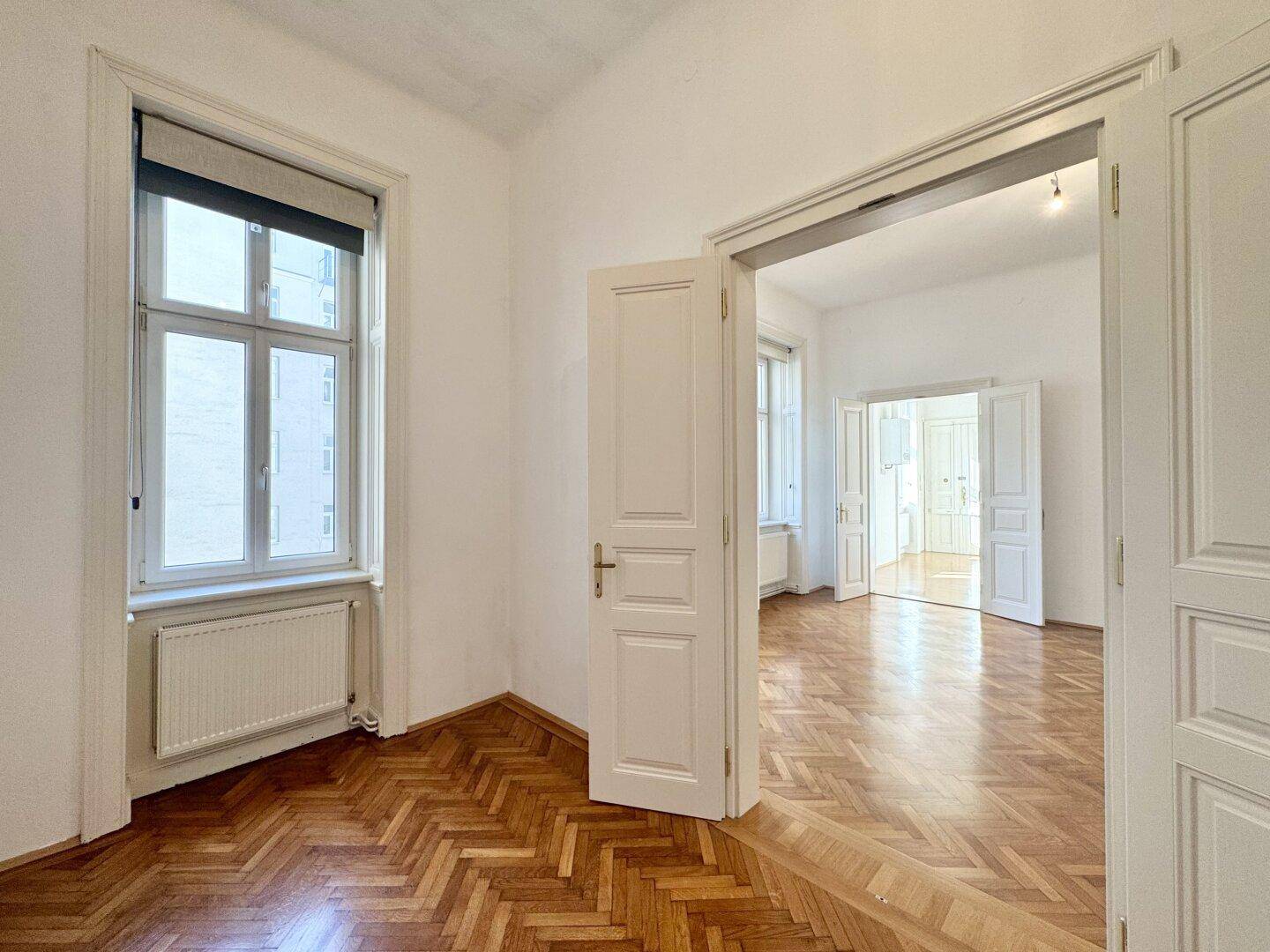Geräumiges Zimmer mit Fischgrätparkettboden und hohen Fenstern, das viel Tageslicht hereinlässt.