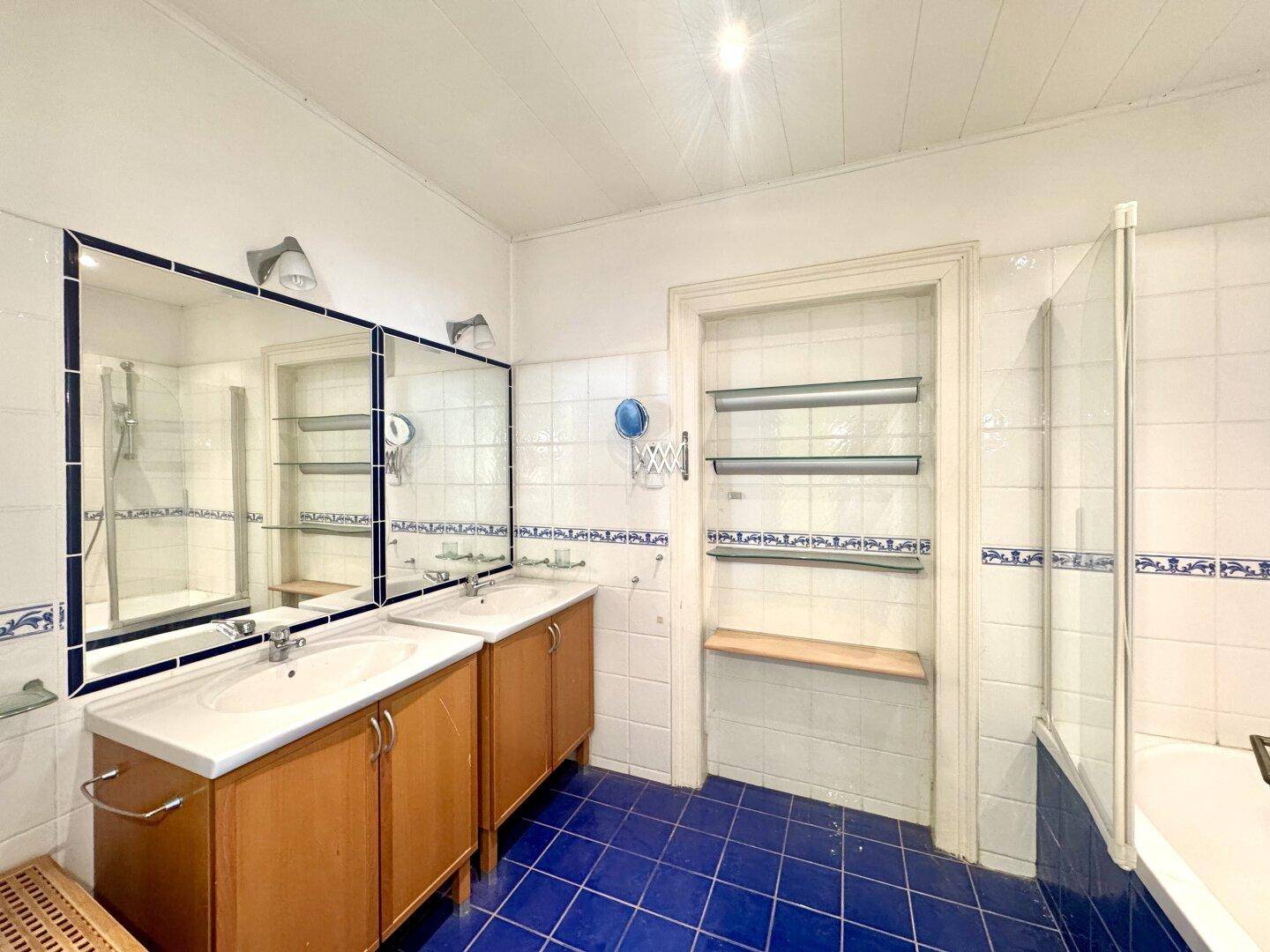 Badezimmer mit Doppelwaschbecken, blauen Fliesen und Badewanne mit Duschabtrennung.