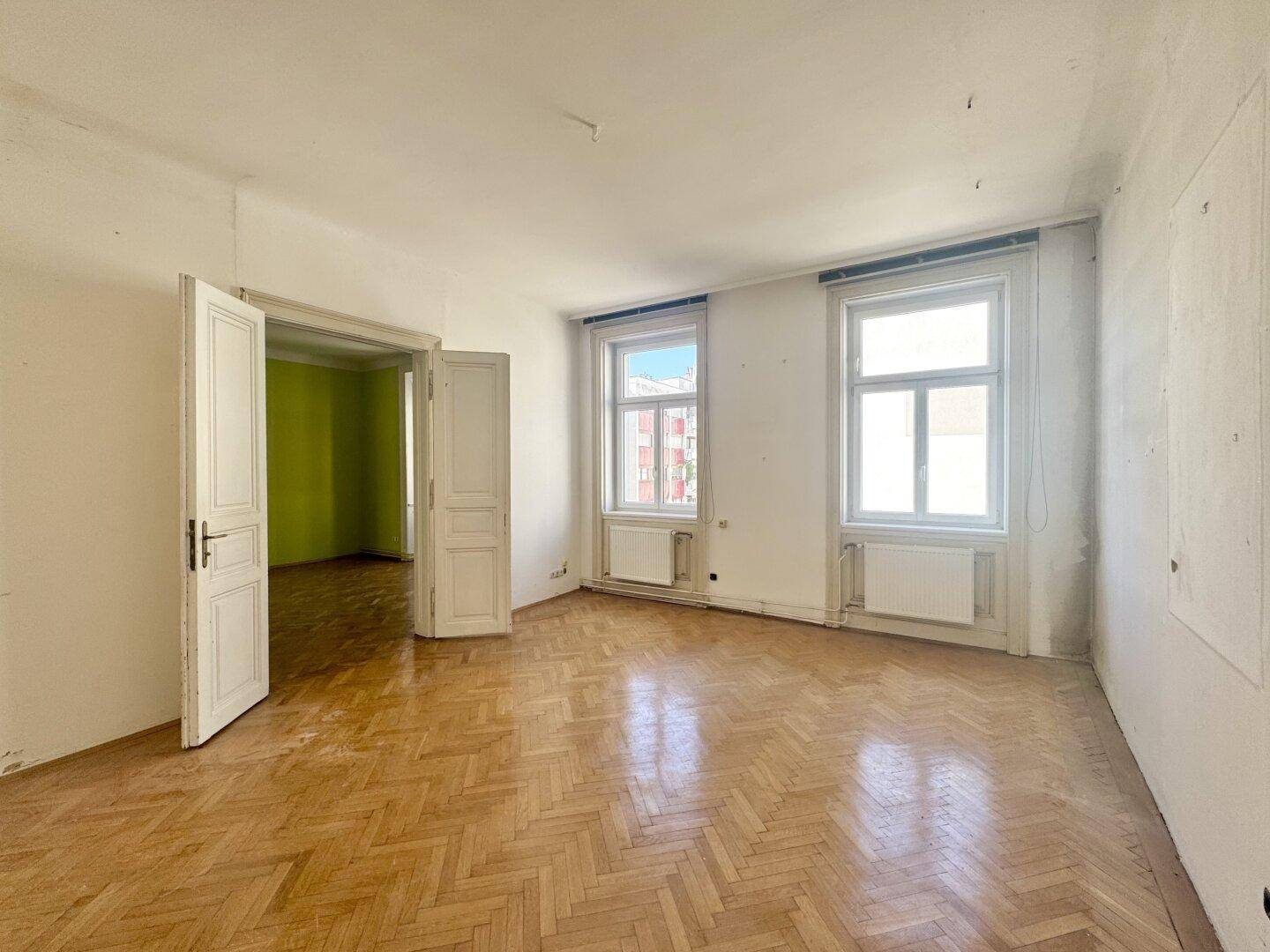 Großes Zimmer mit Fischgrätparkett und hohen Fenstern, ideal für Renovierungsprojekte.