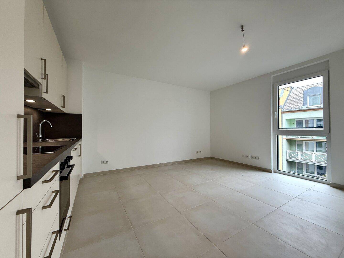 Heller offener Wohnbereich mit integrierter Küche, großem Fenster und Blick nach draußen.