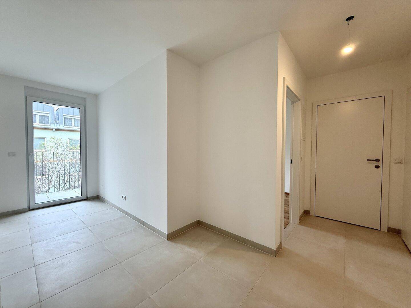 Heller Wohnraum mit Zugang zu einem Balkon und neutralen Fliesenböden.