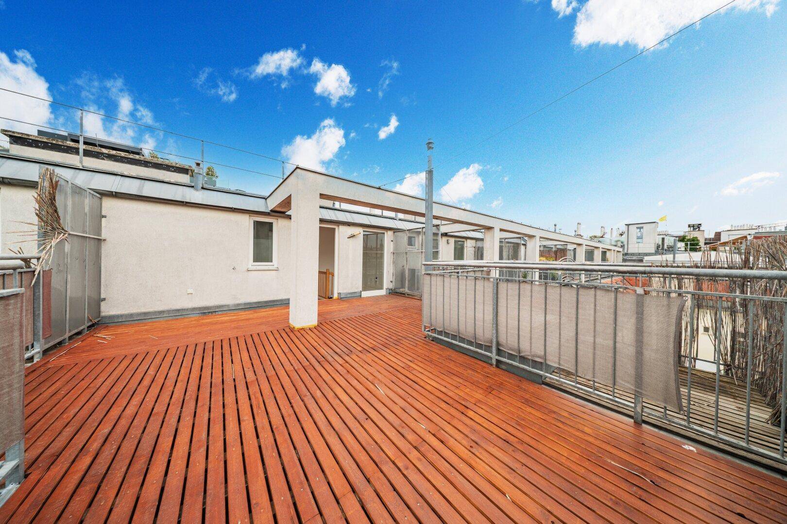 Große Dachterrasse mit Holzboden und Zugang zu den Innenräumen, umgeben von Stadtansichten.