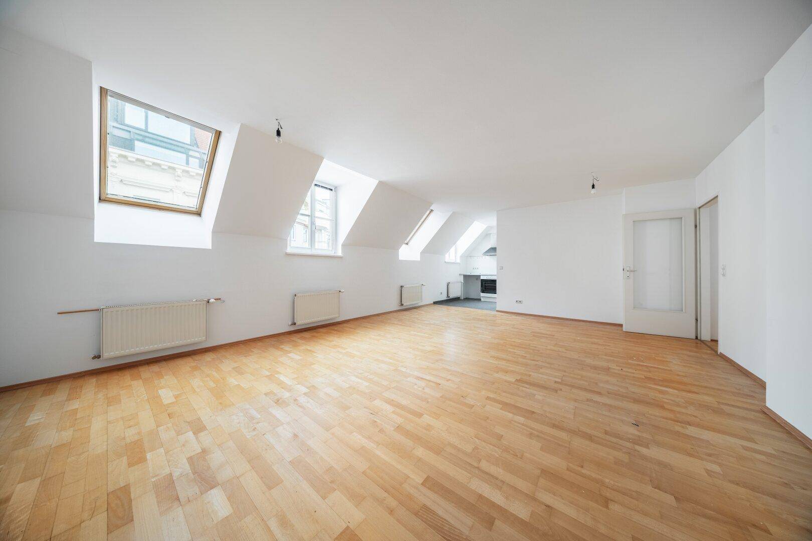 Helles Wohnzimmer mit Dachschrägen, Parkettboden und mehreren Dachfenstern für viel Tageslicht.