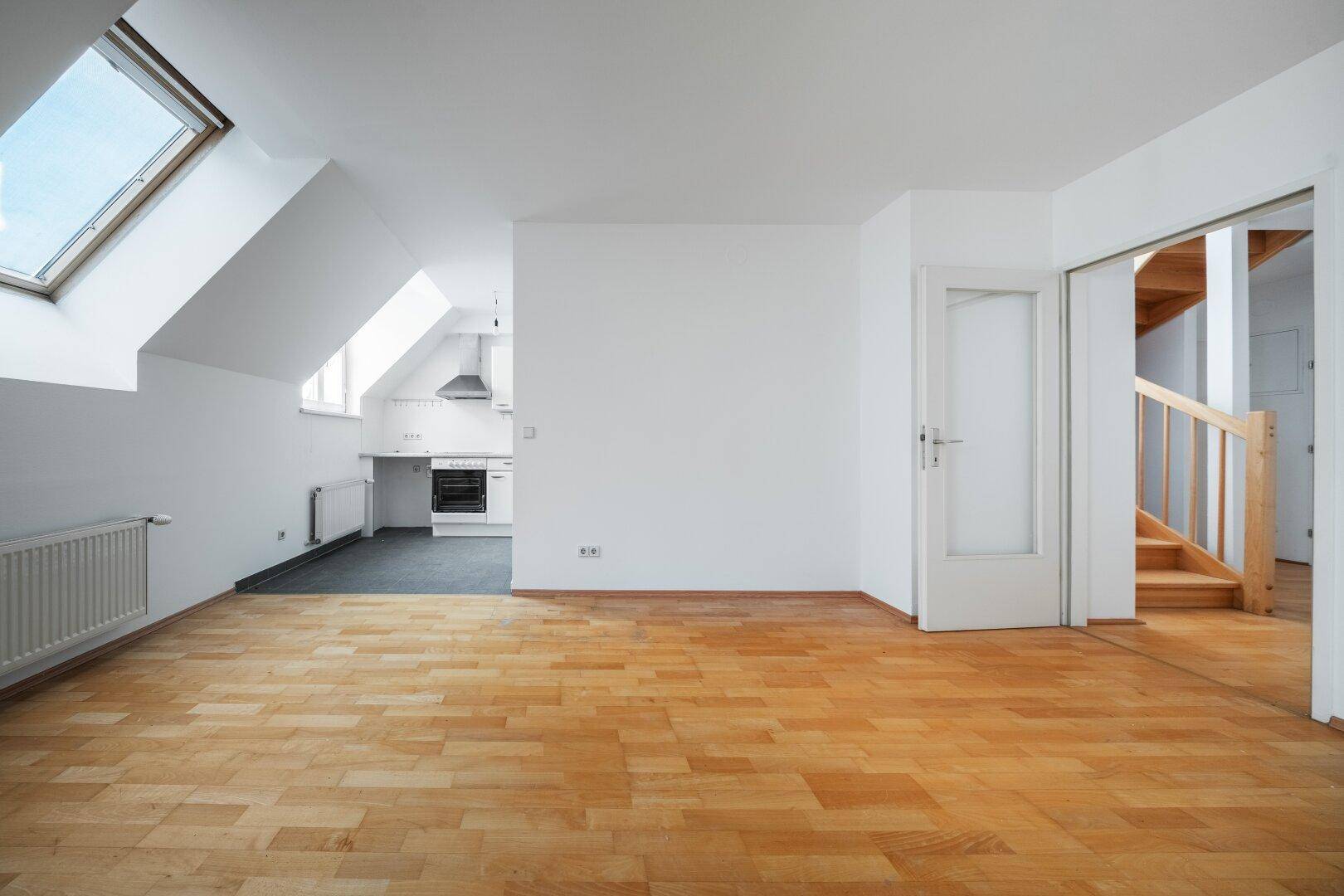 Offener Wohnbereich mit Parkettboden, Dachfenster und Blick auf die angrenzende Küche.