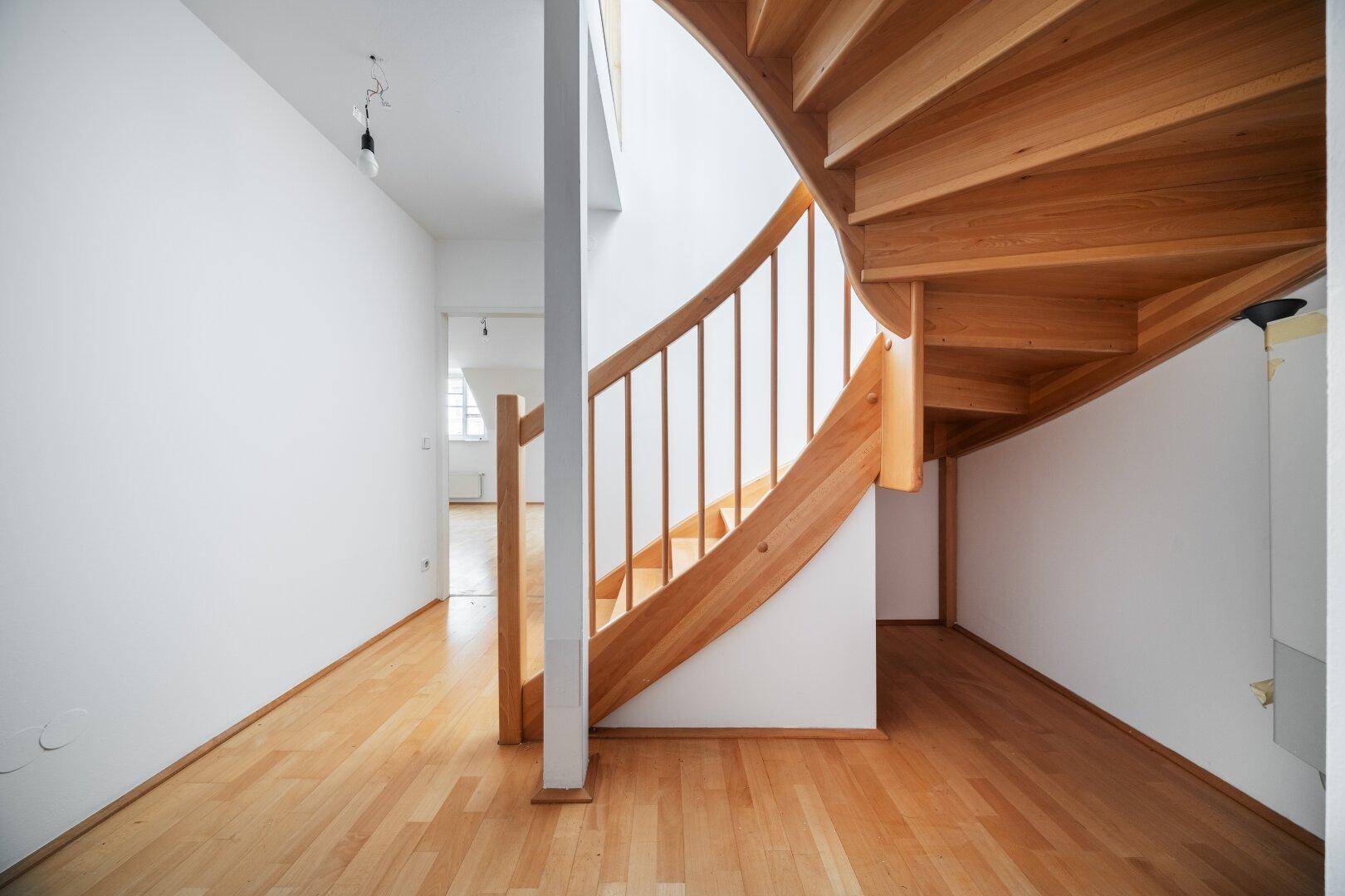 Heller Flur mit geschwungener Holztreppe und Parkettboden, der verschiedene Ebenen verbindet.