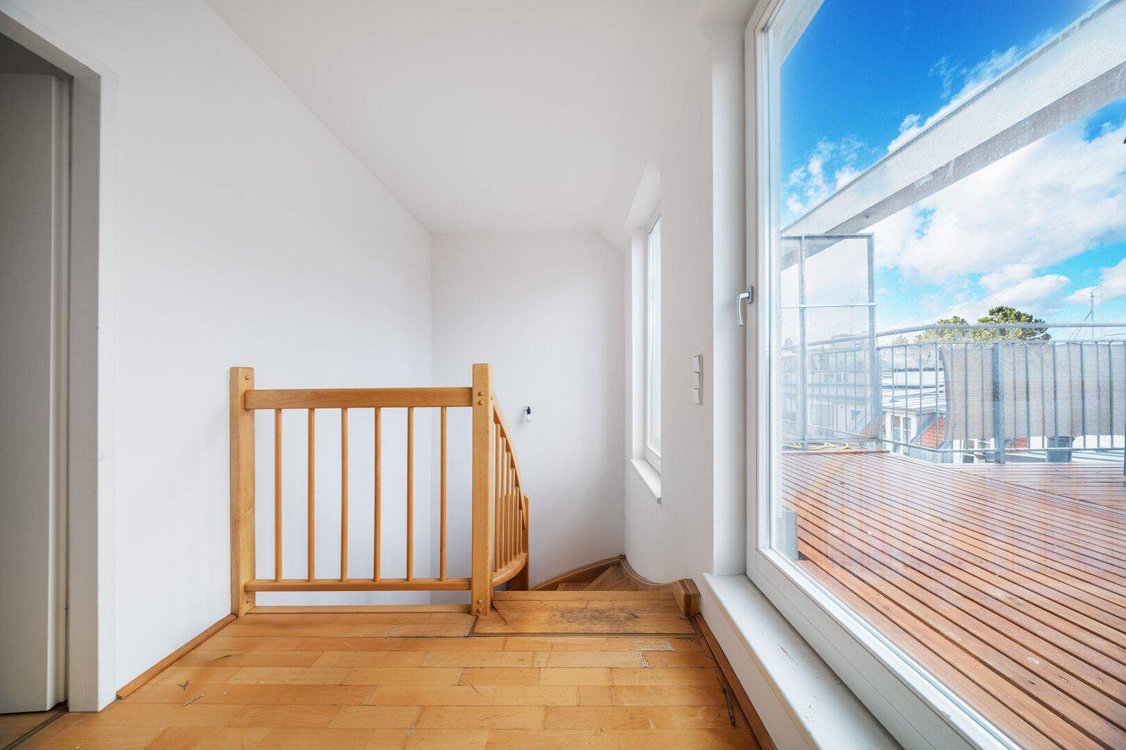 Heller Treppenabsatz mit Holzboden und direktem Zugang zur sonnigen Dachterrasse.