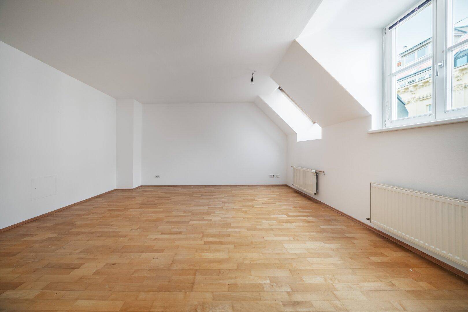 Geräumiges Schlafzimmer mit Dachschrägen, Parkettboden und großen Fenstern für viel Licht.