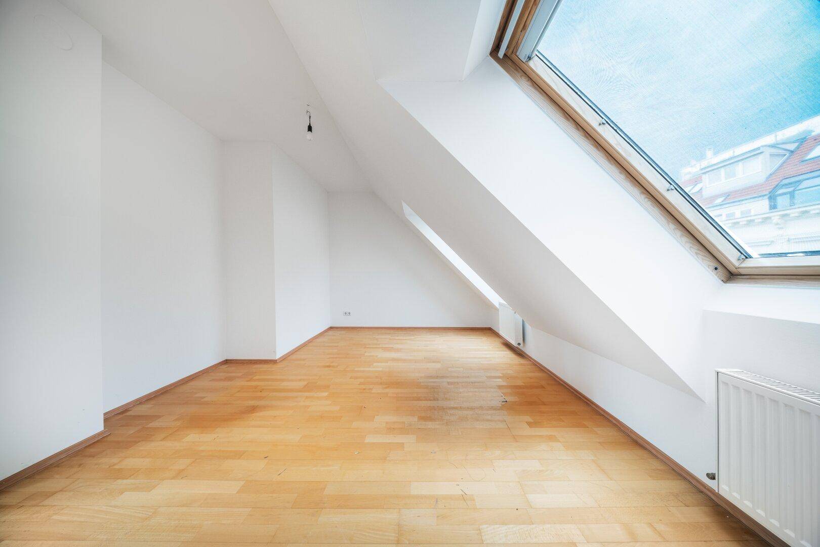 Helles Schlafzimmer mit Dachschrägen, Parkettboden und einem großen Dachfenster.