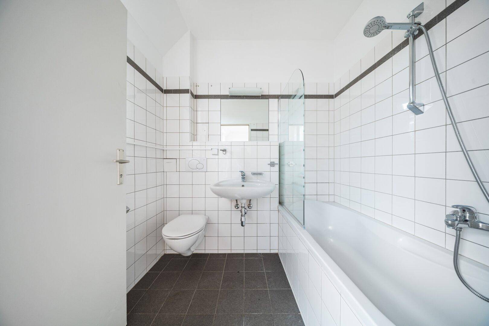 Funktionales Badezimmer mit weißen Fliesen, Badewanne mit Duschfunktion und Waschbecken.