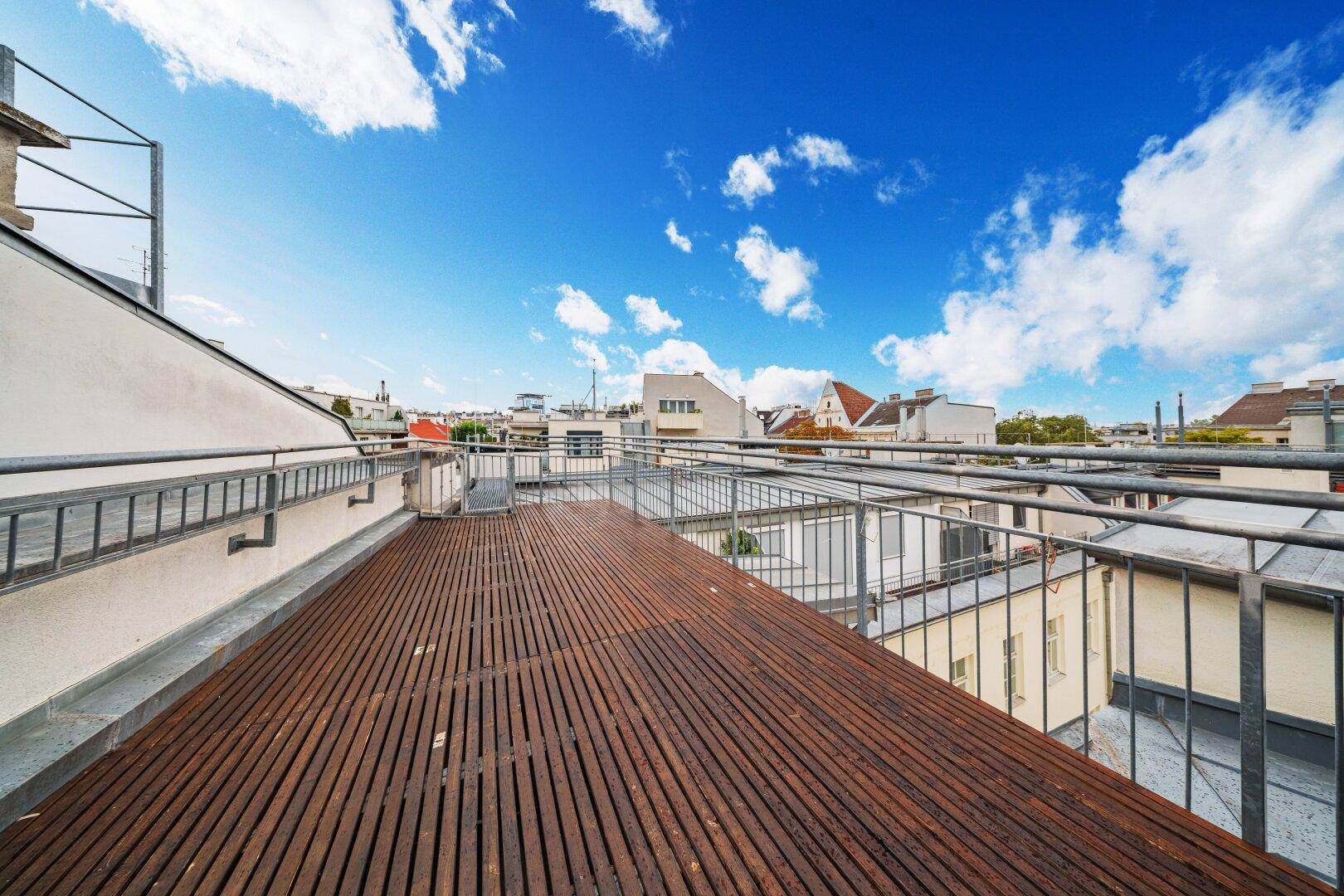Geräumige Dachterrasse mit Holzbelag und weitem Blick auf die städtische Umgebung.