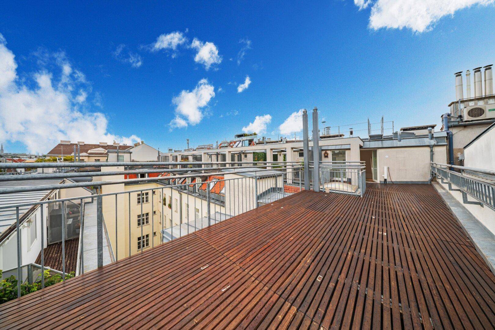 Weitläufige Dachterrasse mit Holzplanken und Panoramablick über die Dächer der Stadt.