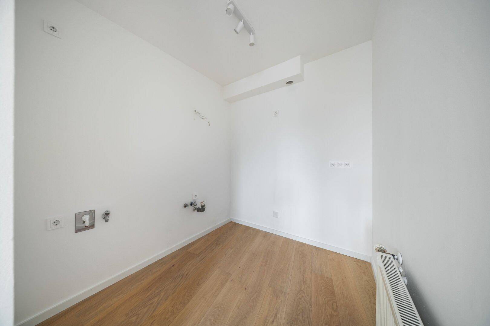 Kleiner Raum mit Holzboden und Anschlüssen für Sanitärinstallationen oder eine Küche.
