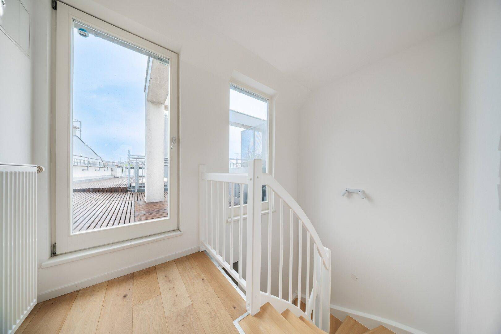 Treppenaufgang mit Holzboden und Zugang zur Dachterrasse durch eine große Glastür.