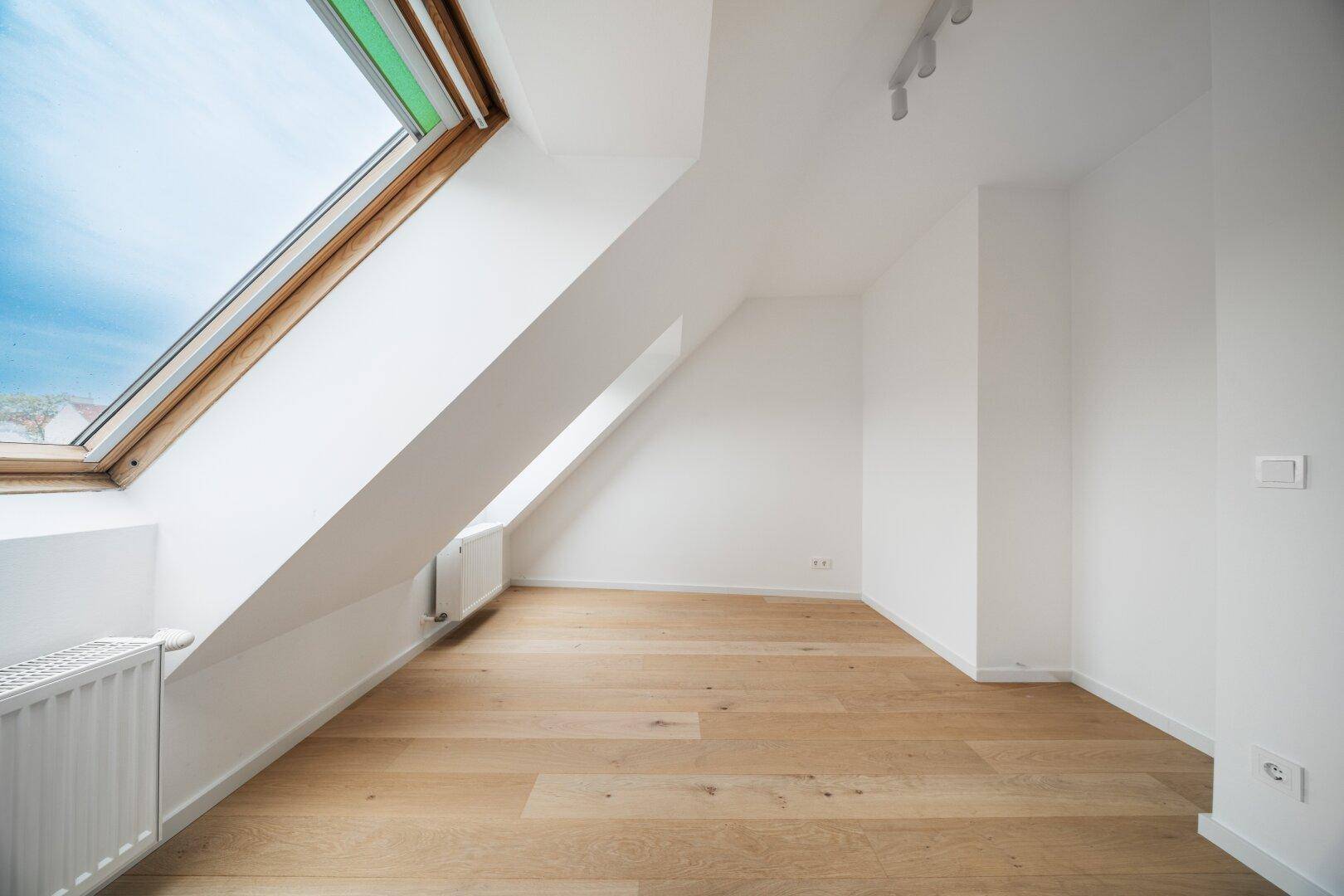 Geräumiges Zimmer mit Holzboden, Dachschräge und großem Dachfenster für viel Licht.