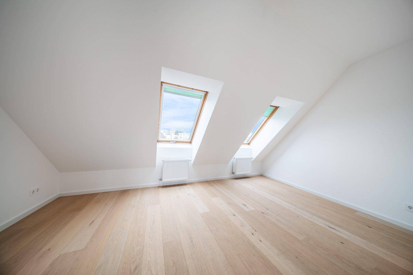 Helles Zimmer mit Holzboden, Dachschrägen und zwei Dachfenstern, die viel Licht spenden.