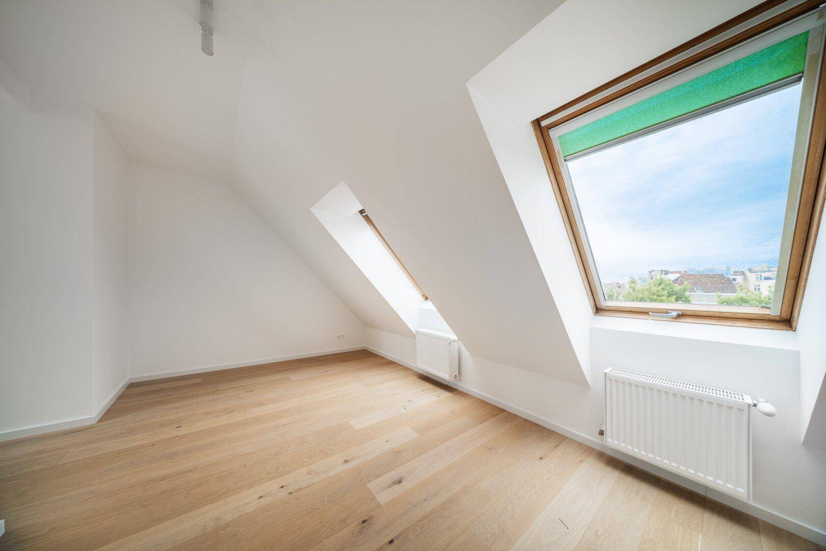 Lichtdurchflutetes Zimmer mit Holzboden, Dachschräge und großem Dachfenster mit Ausblick.