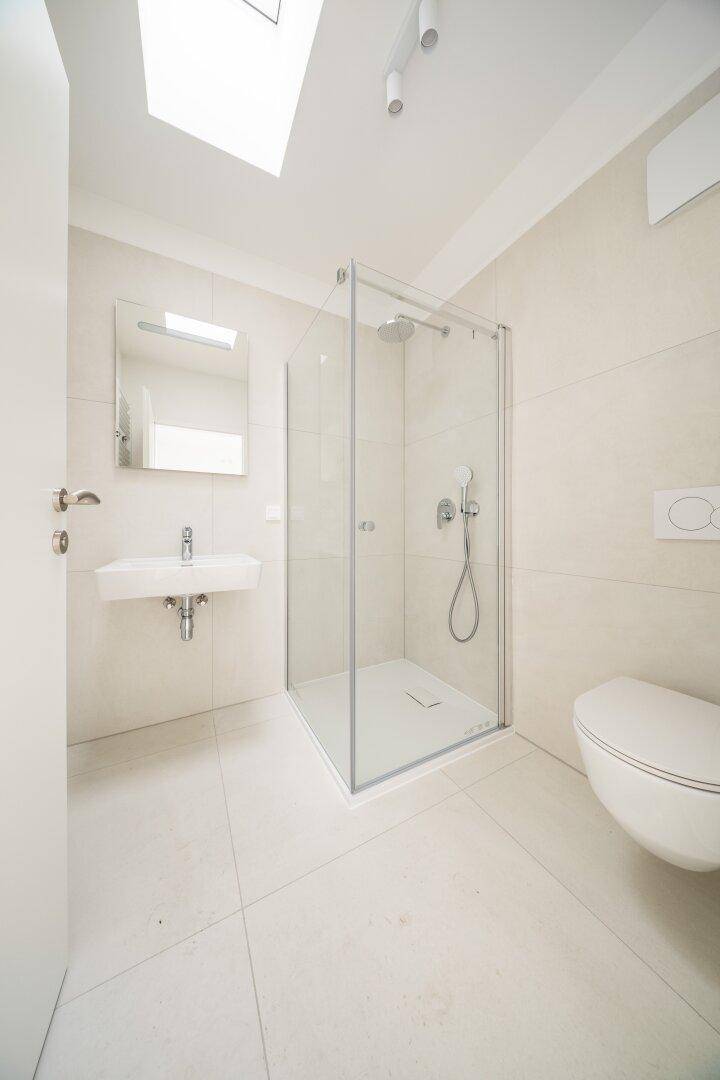 Modernes Badezimmer mit beigefarbenen Fliesen, Duschkabine und wandhängendem WC.