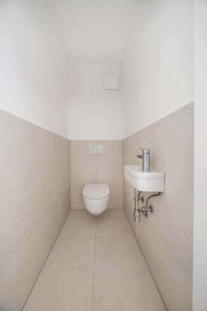Kleines Gäste-WC mit beigefarbenen Fliesen, wandhängendem WC und Handwaschbecken.