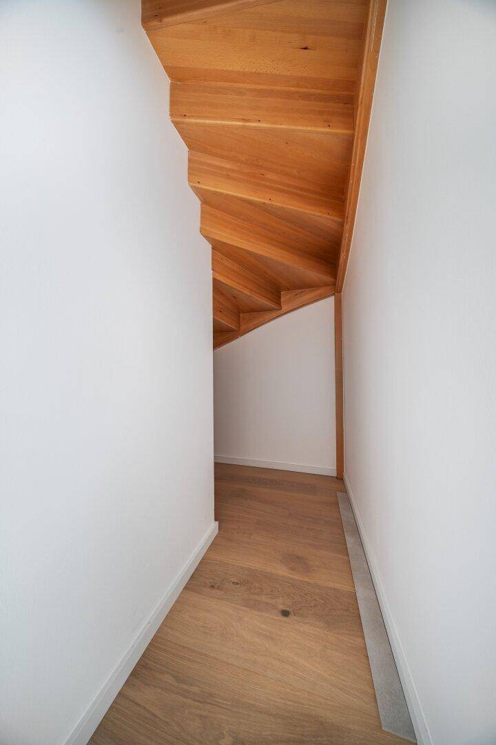 Schmaler Durchgang mit Holzboden und sichtbarer Holzunterkonstruktion der Treppe.