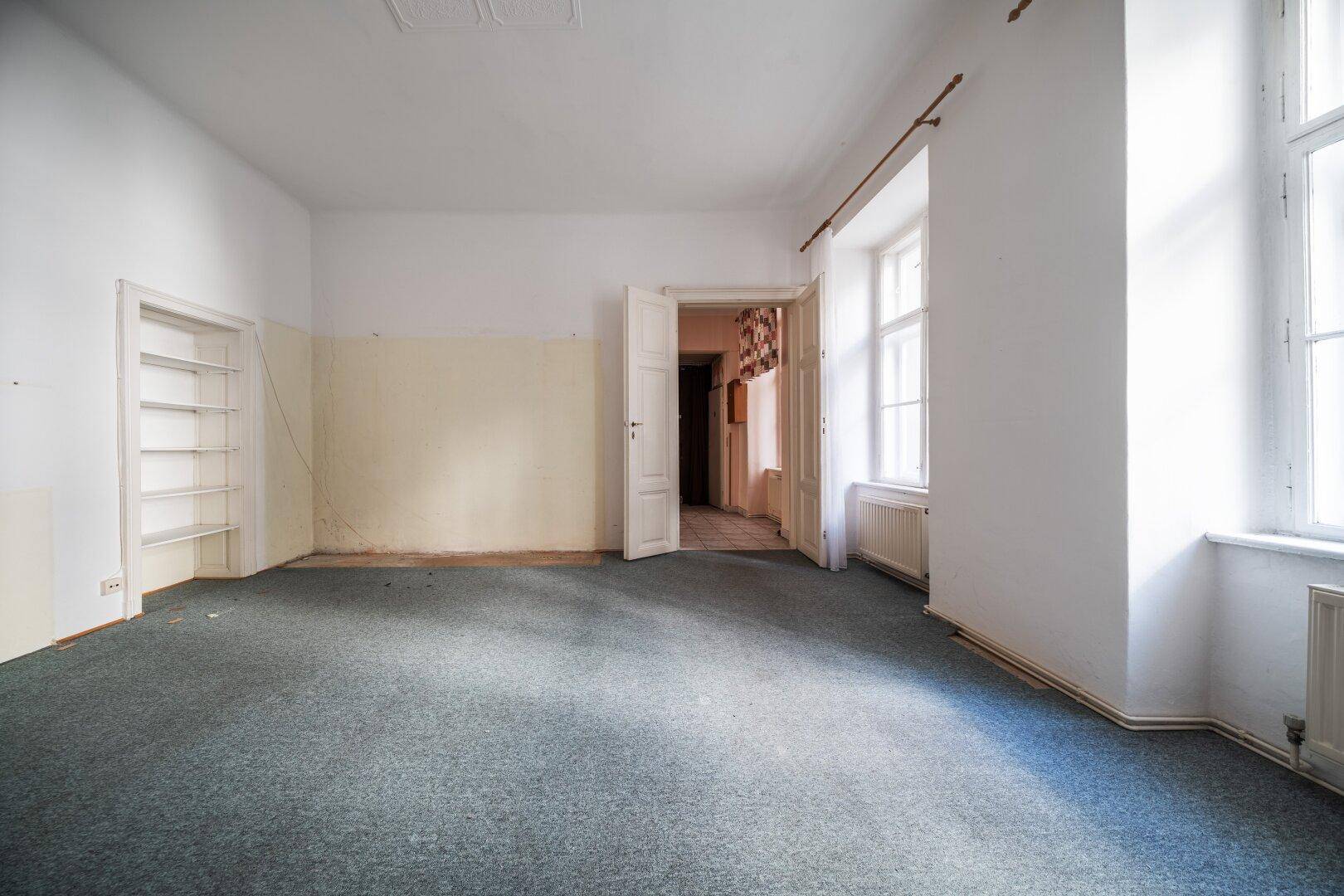 Unmöblierter Raum mit grauem Teppichboden, weißen Wänden und einem eingebauten Regal.