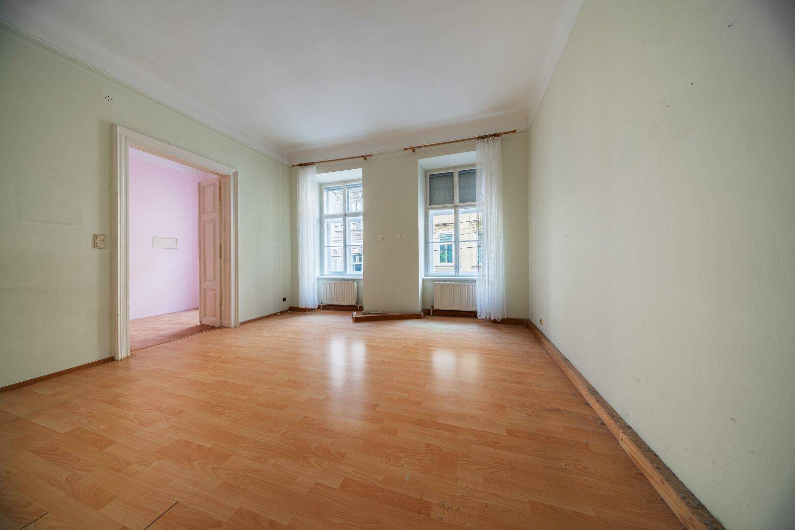 Heller, unmöblierter Raum mit hellem Laminatboden und Fenstern mit Blick auf die Stadt.