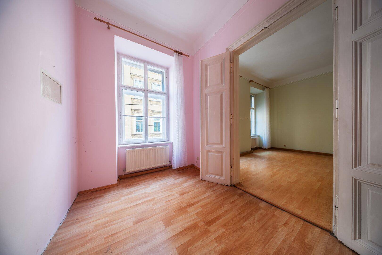 Unmöblierter Raum mit rosa Wänden, Laminatboden und einem Fenster mit Blick auf die Straße.
