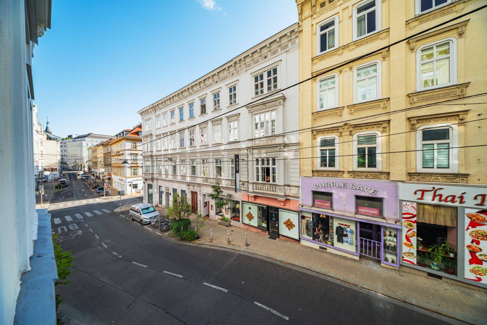 Blick von oben auf eine belebte Stadtstraße mit historischen Gebäuden und Geschäften.