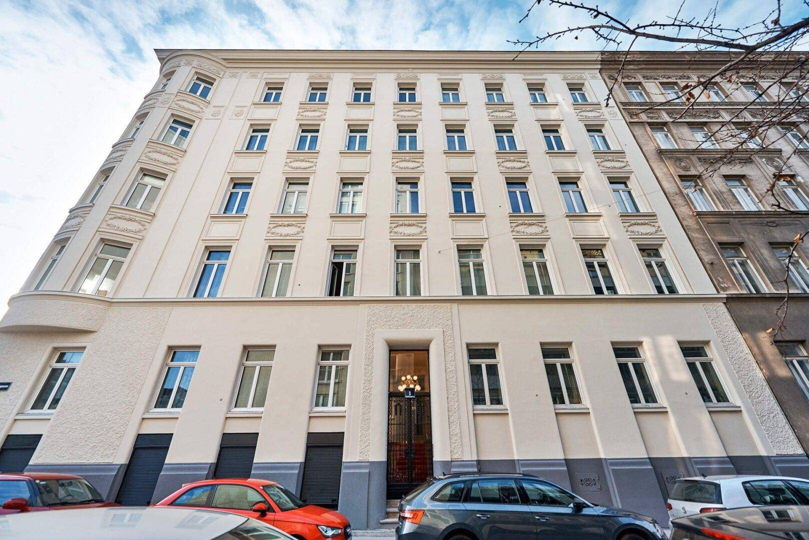 Elegante Fassade eines Mehrfamilienhauses mit vielen Fenstern und klassischem Eingangsbereich.